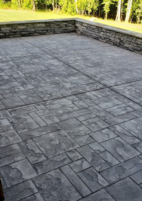 Stamped concrete slab with stone pattern finish bordered by a stacked stone wall